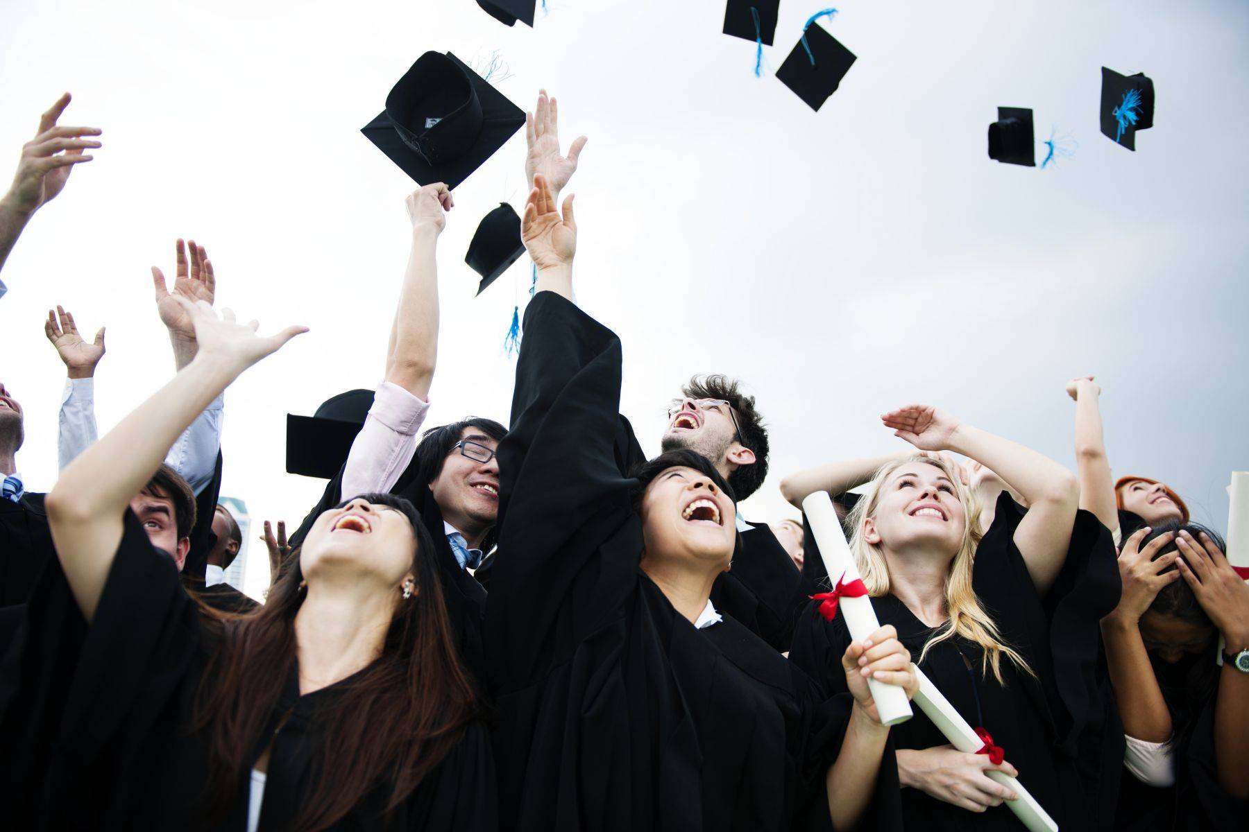 group-diverse-grads-throwing-caps-up-sky